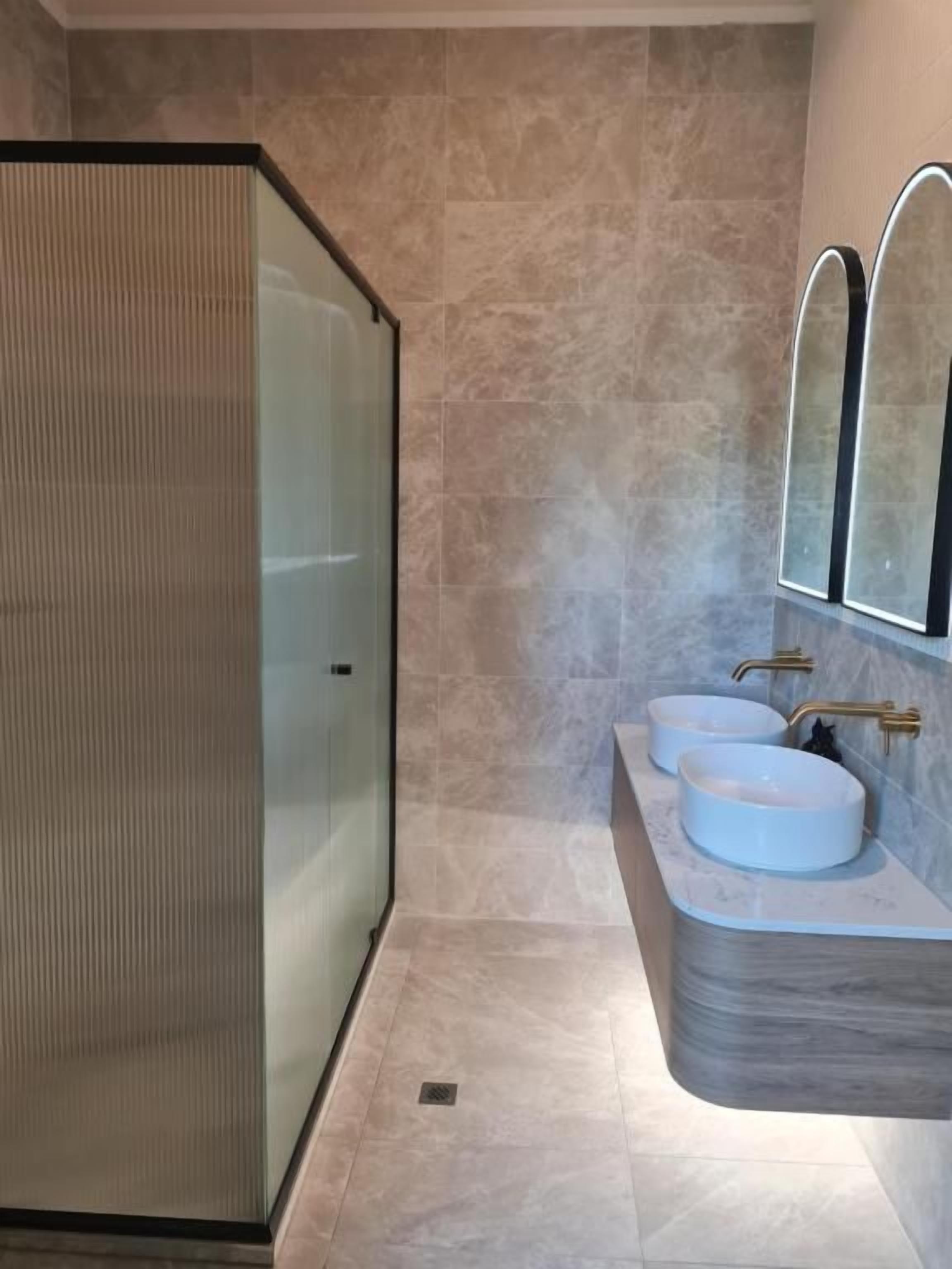Une salle de bain moderne avec une douche à parois de verre, deux vasques aux formes arrondies et un sol carrelé en marbre.