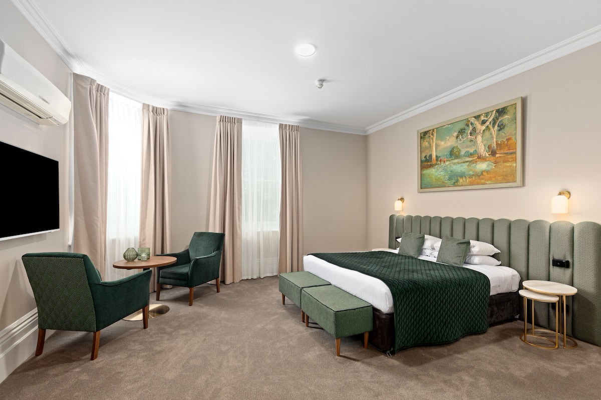 A hotel room with a bed, two armchairs, a small table, and a painting on the wall.