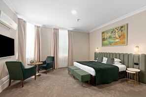 Una habitación de hotel con una cama, dos sillones, una mesita y un cuadro en la pared.