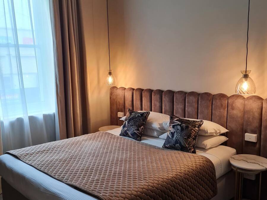 A neatly made bed with a brown quilt, two pillows, and a bedside table with a lamp.