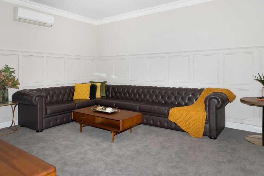 A room with a dark brown leather sofa, a wooden coffee table, and a small round table with a plant.