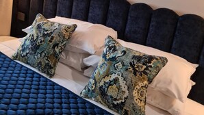A hotel room with a large bed, a headboard with a unique design, a wall-mounted mirror, and a wall-mounted light fixture.