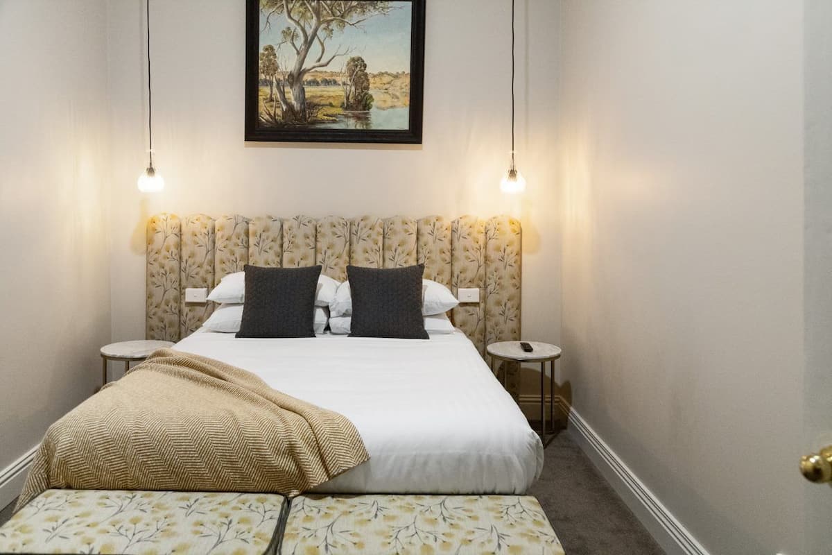 A neatly arranged bedroom with a bed, bedside tables, a bench, and a painting on the wall.