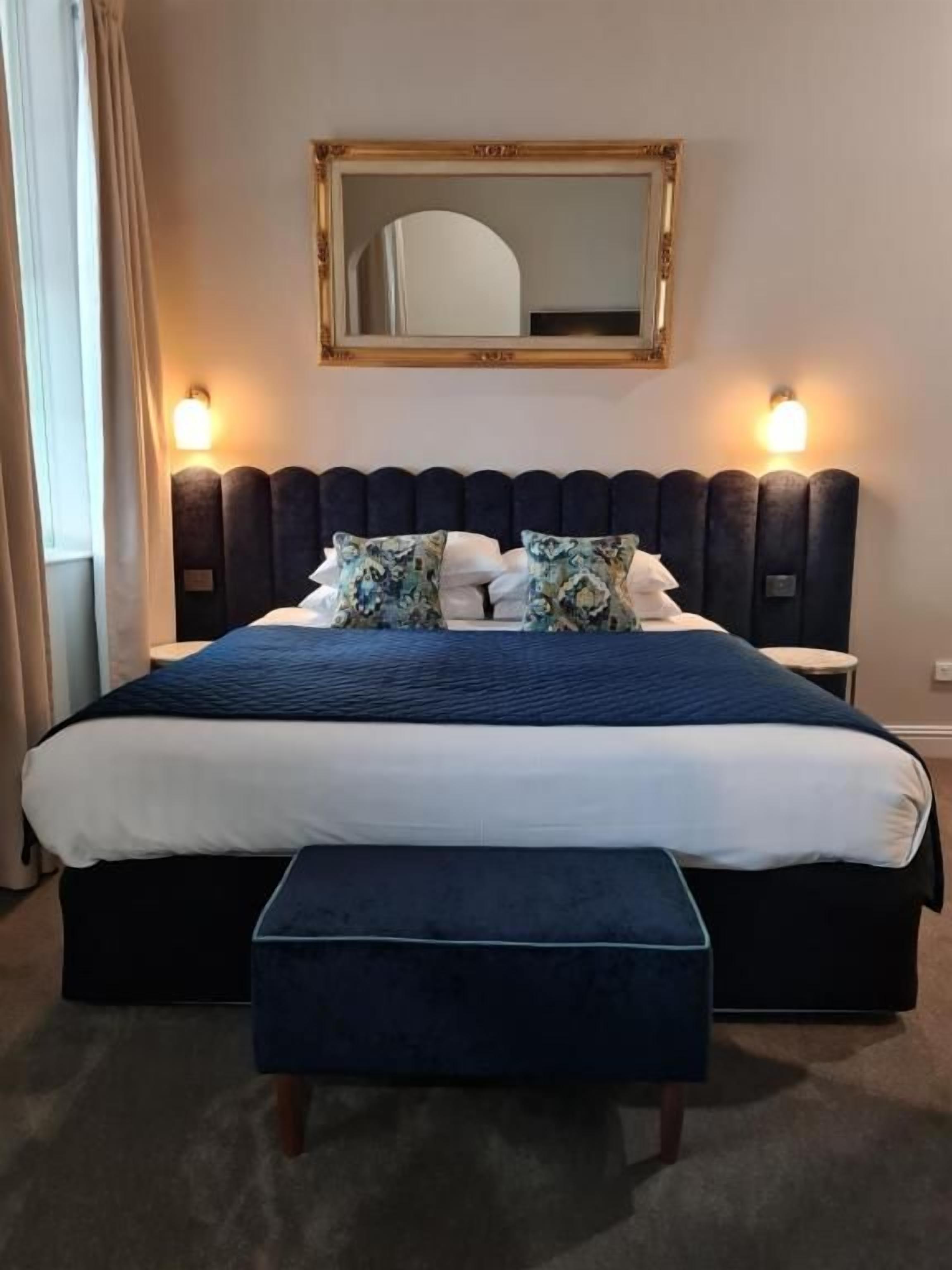 Une chambre d’hôtel standard, comprenant un lit, des tables de chevet, un banc et un miroir.