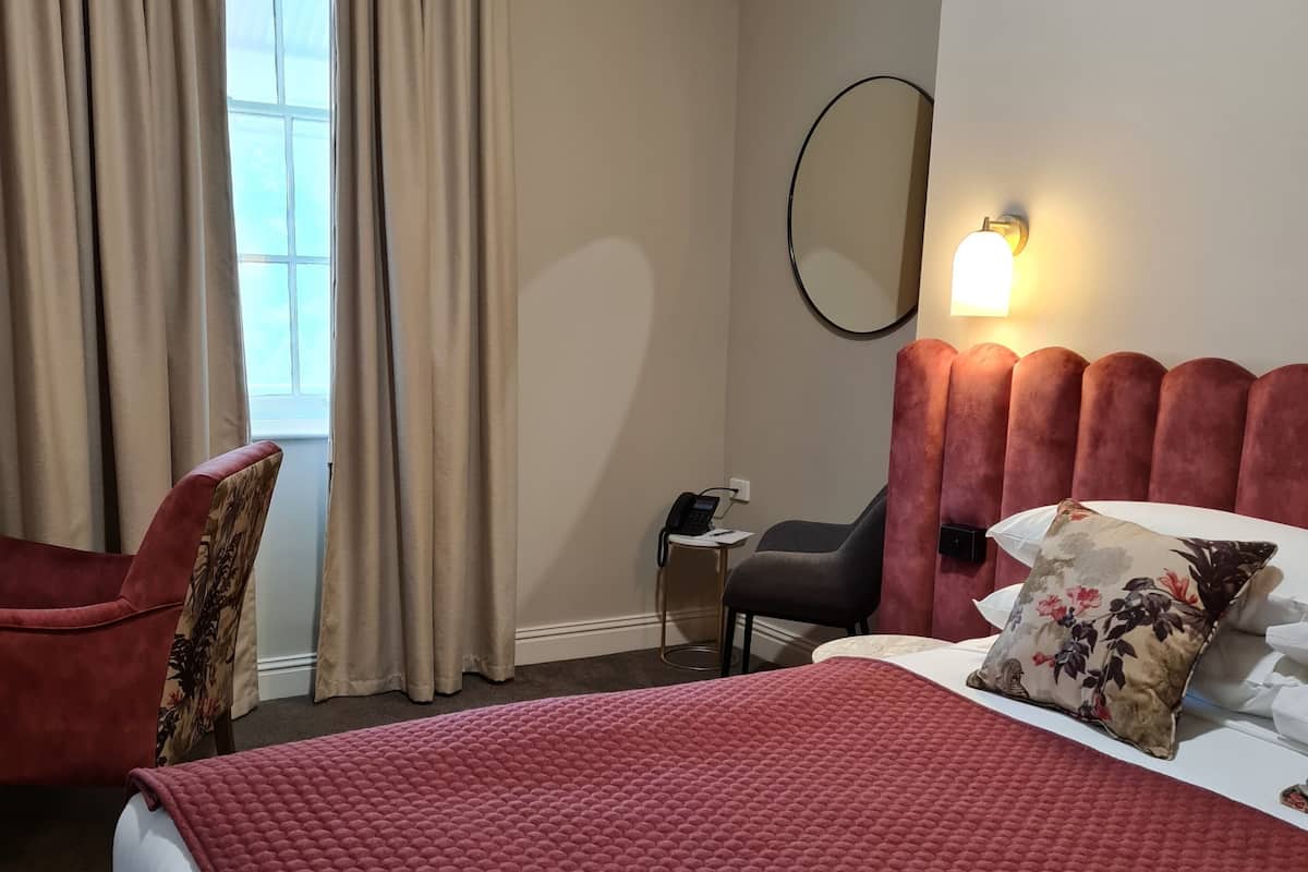 A hotel room with a large bed, a chair, a small table, a phone, and a wall-mounted light.