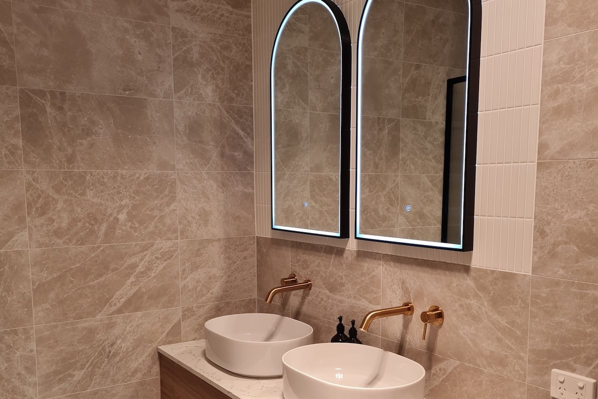 A modern bathroom with two sinks, a wooden vanity, and two wall-mounted mirrors with illuminated frames.