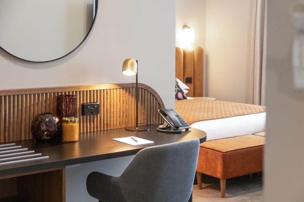 Habitación de hotel con escritorio, una silla, cama, lámpara de noche y teléfono instalado en la pared.