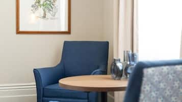 Una stanza con una poltrona blu, un tavolo rotondo in legno e una stampa botanica incorniciata appesa al muro.