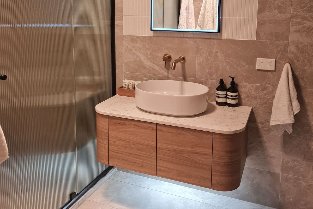 A modern bathroom with a round sink, wooden vanity, and a large mirror with an illuminated frame.