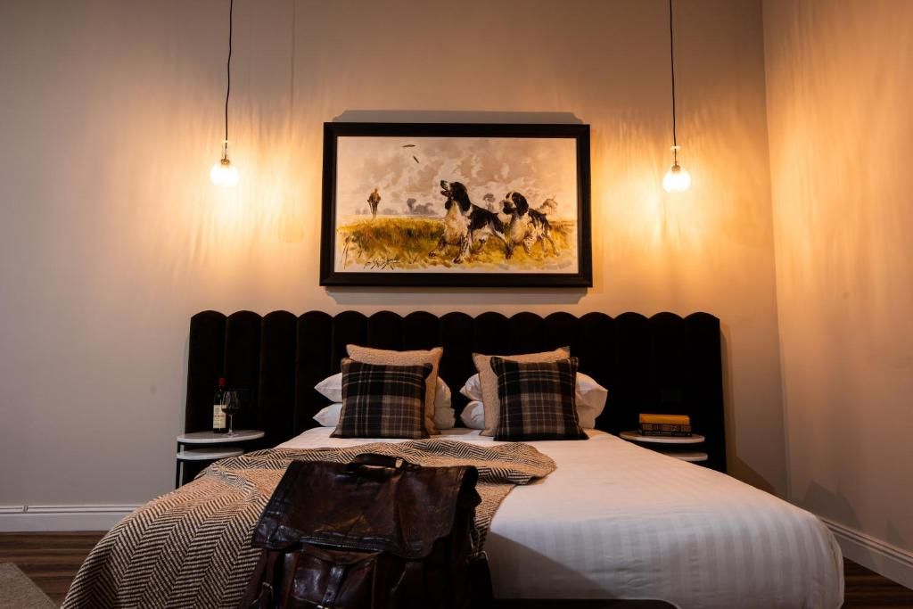 A hotel room with a bed, a painting, two bedside lamps, a nightstand, and a handbag on the bed.