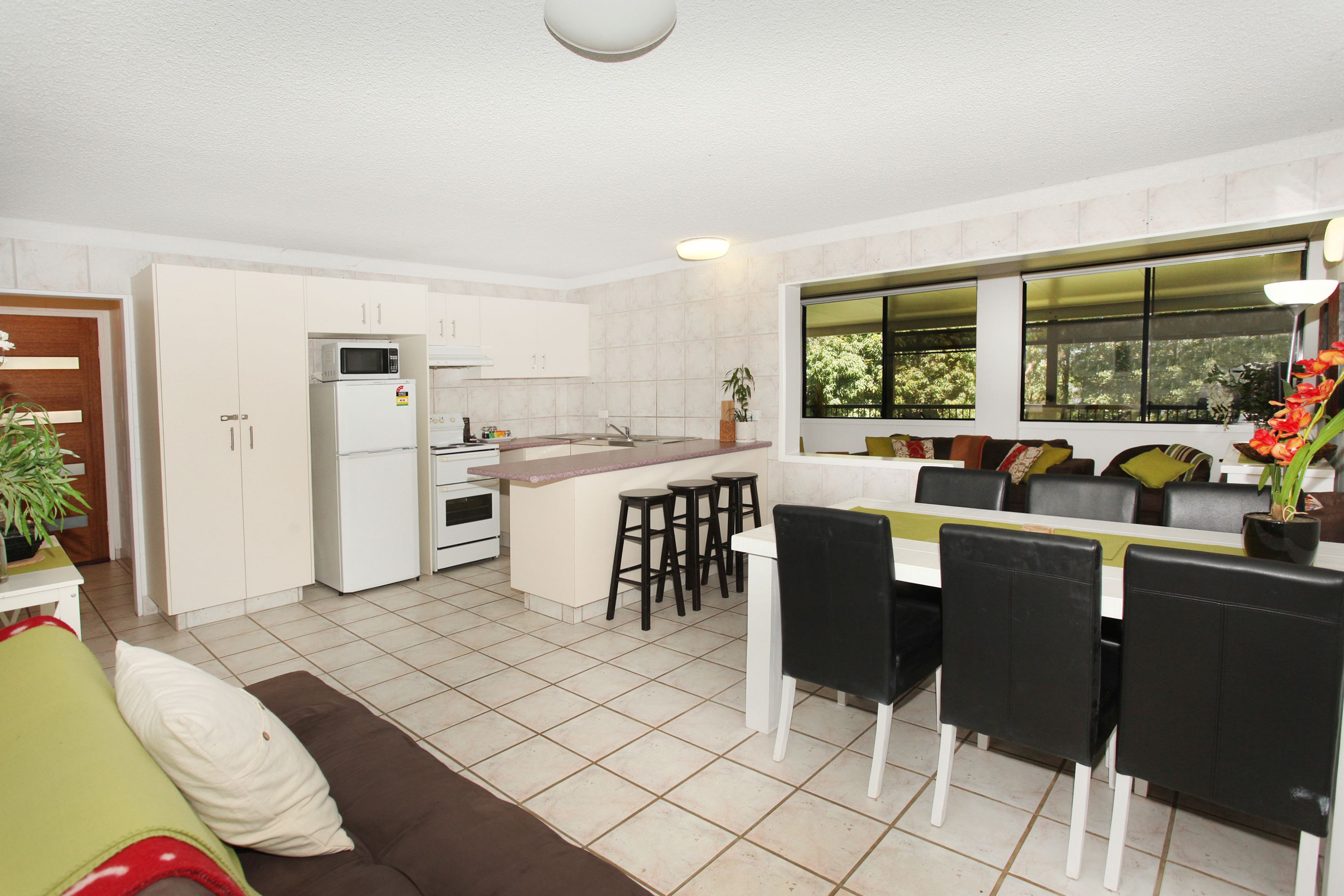 A modern kitchen with white cabinets, a built-in microwave, and a dining area with a white table and black chairs.