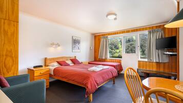 A hotel room with two single beds, a wooden table, a chair, a TV, and a window with curtains.