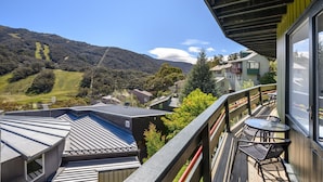 A balcony with a table and chairs, overlooking a hilly landscape with houses. - Kasees Apartments & Mountain Lodge (Thredbo)