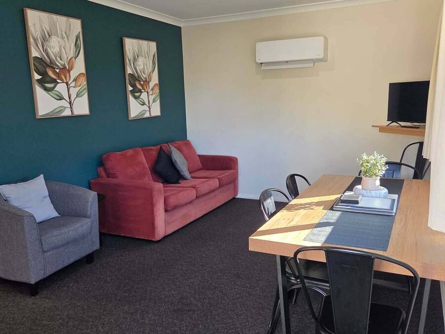 A room with a red sofa, a grey armchair, a wooden dining table with chairs, and two wall-mounted air conditioning units.