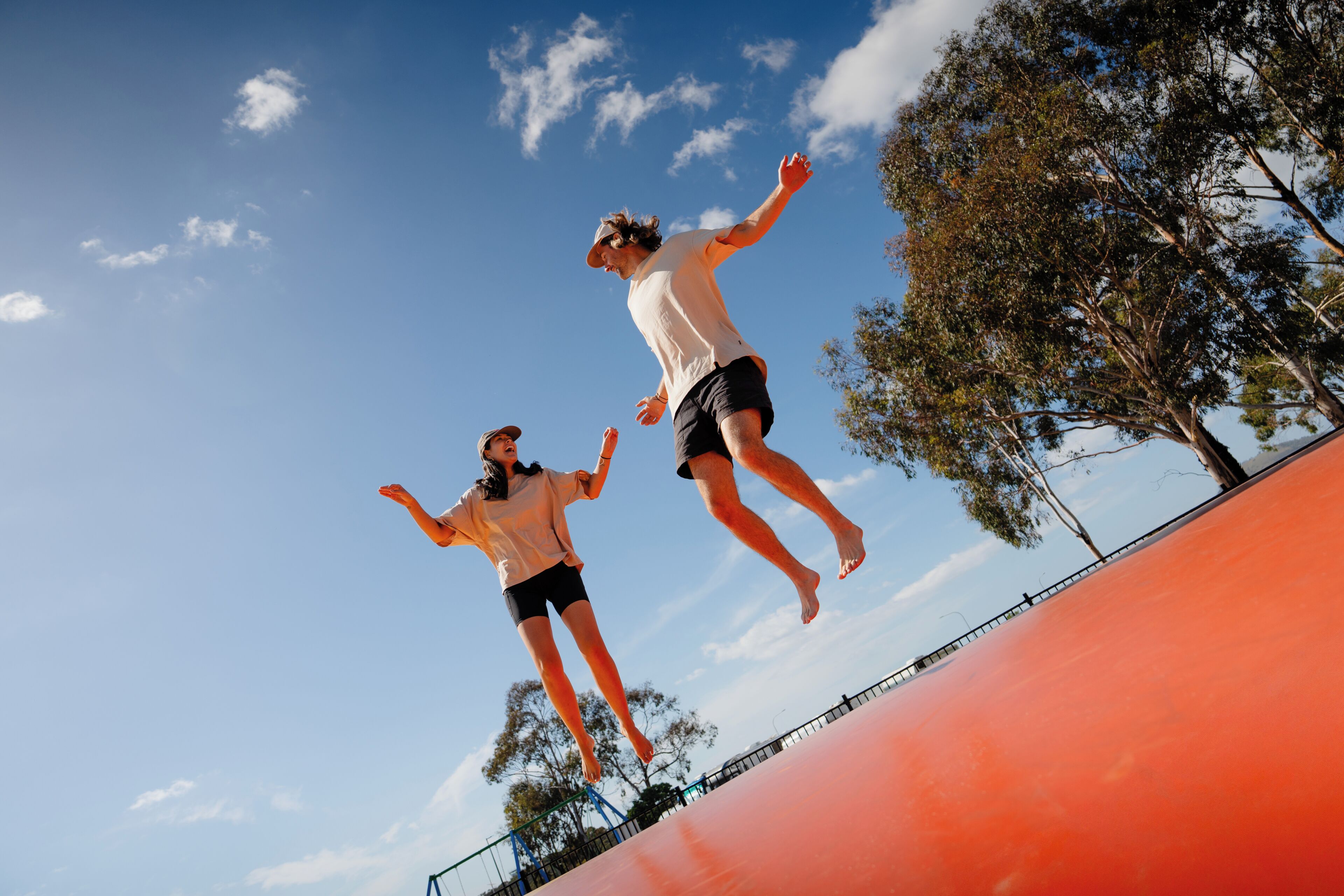 Dos personas saltando en un trampolín, con un cielo despejado y árboles al fondo.