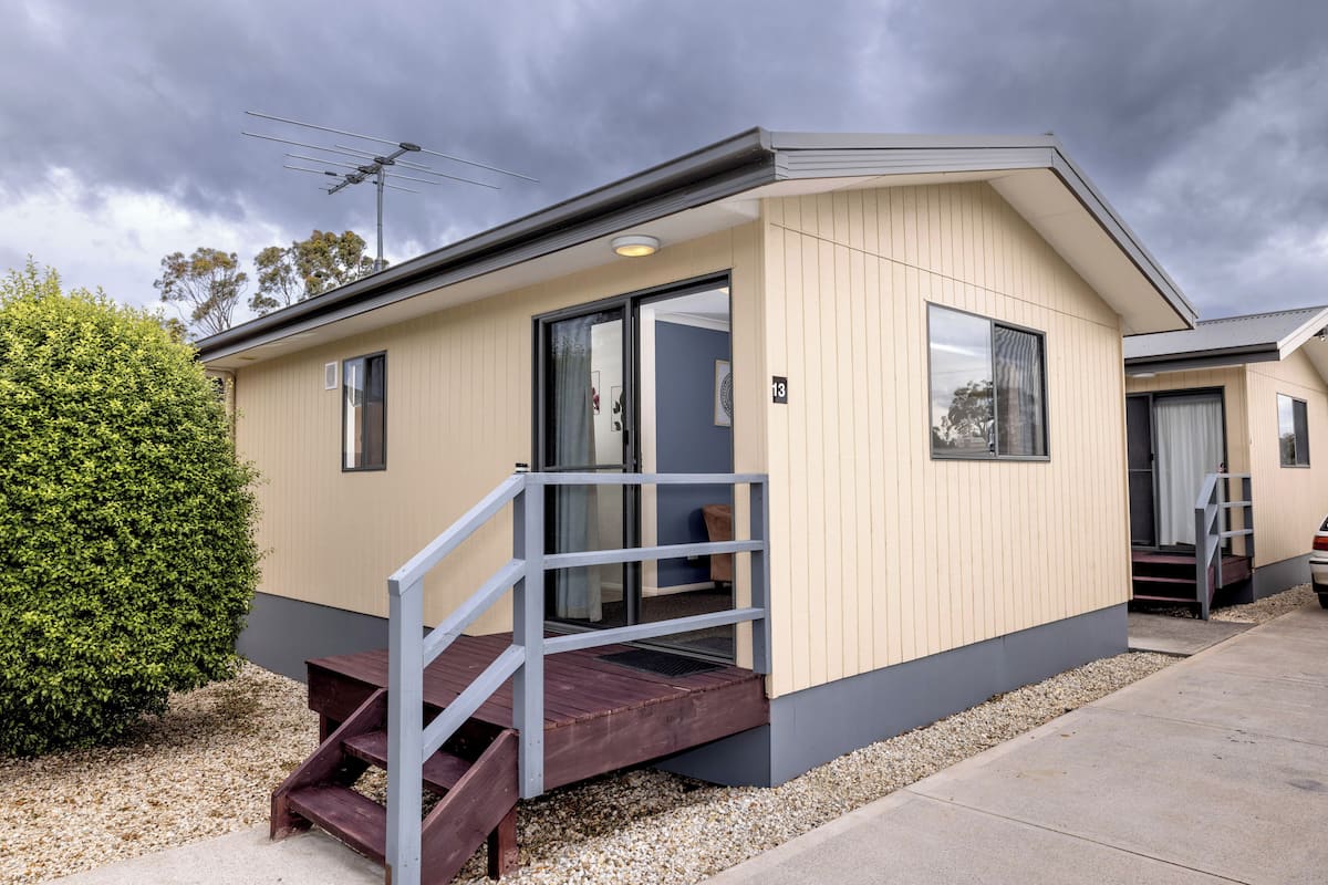 A modern single-story house with a wooden deck, a small porch, and a visible number '13' on the side.