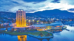 A high-rise hotel with a central courtyard and waterfront views, surrounded by a cityscape and mountains. - BIG4 Hobart Airport Tourist Park (Cambridge)