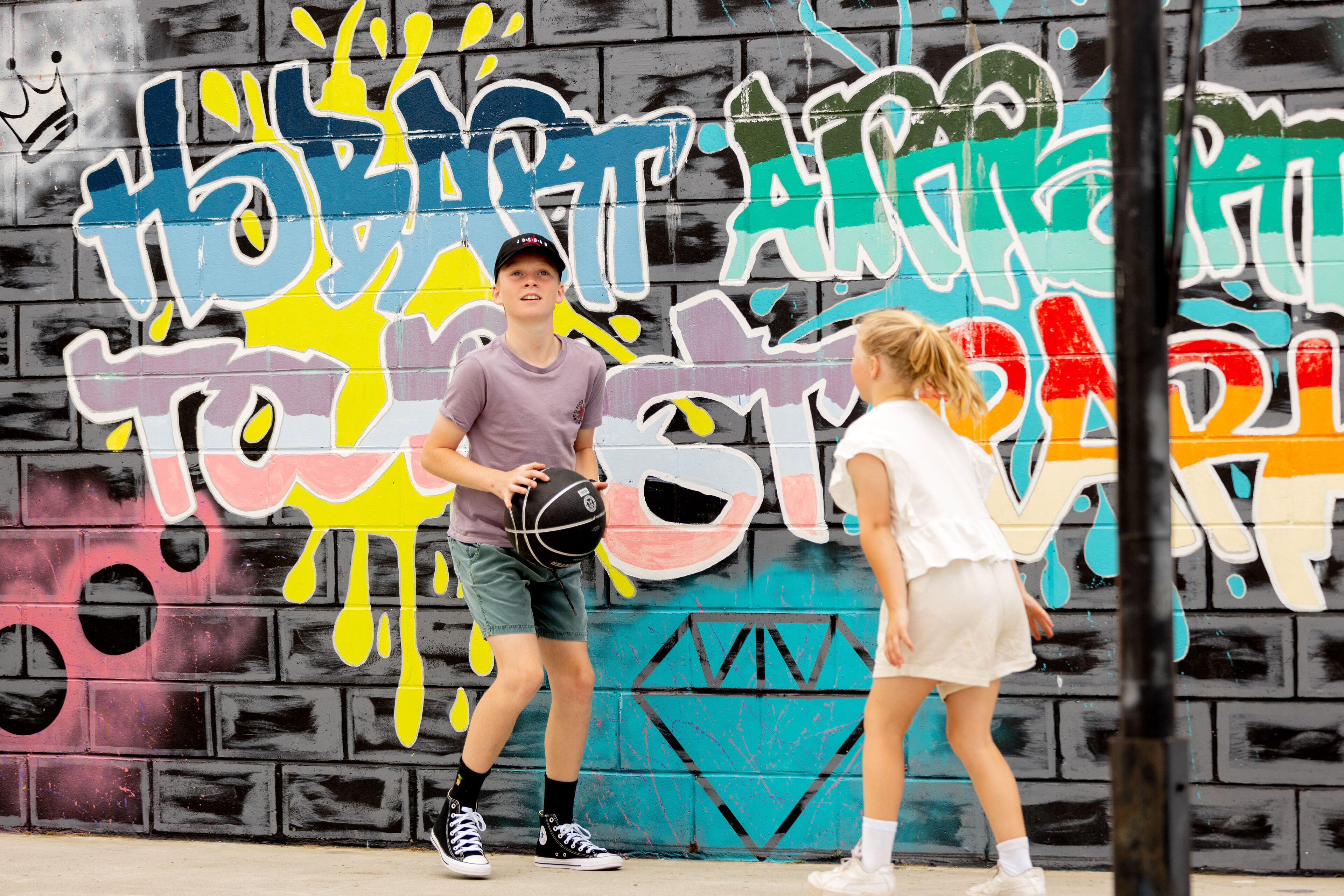 Two people playing basketball in front of a graffiti-covered wall.