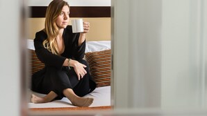 Une personne est assise sur un lit dans une pièce où un tableau abstrait aux couleurs vives est accroché au mur.