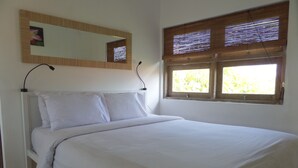 Un dormitorio con cama, ventana con marco de madera y persianas, espejo fijado a la pared y un cuadro de una flor.