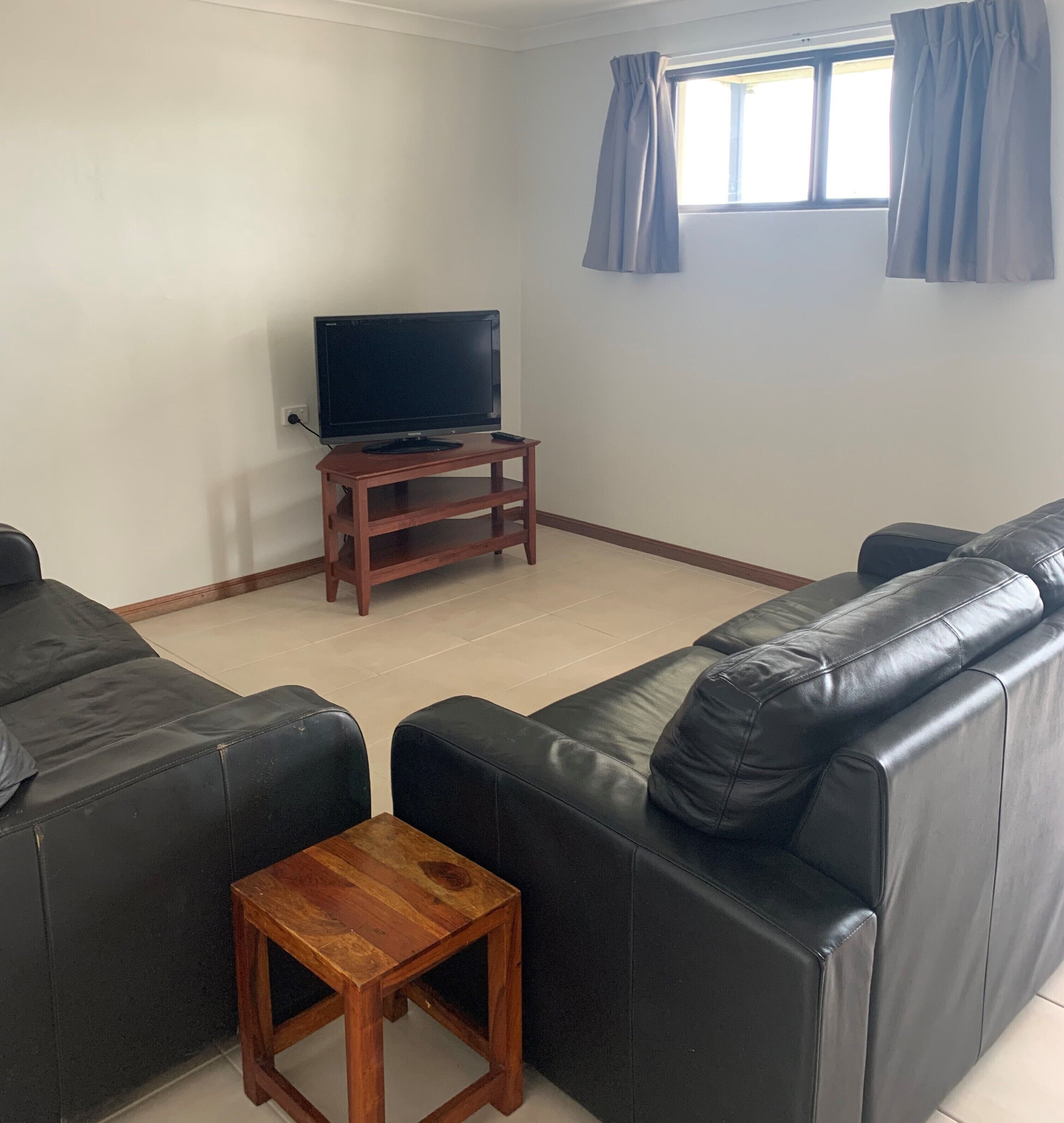 A living room with a black leather sofa, a wooden coffee table, and a TV on a stand.