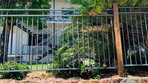 A stone wall with a metal fence, a staircase, and a building with a balcony. - Airlie Beach Apartments (Airlie Beach)