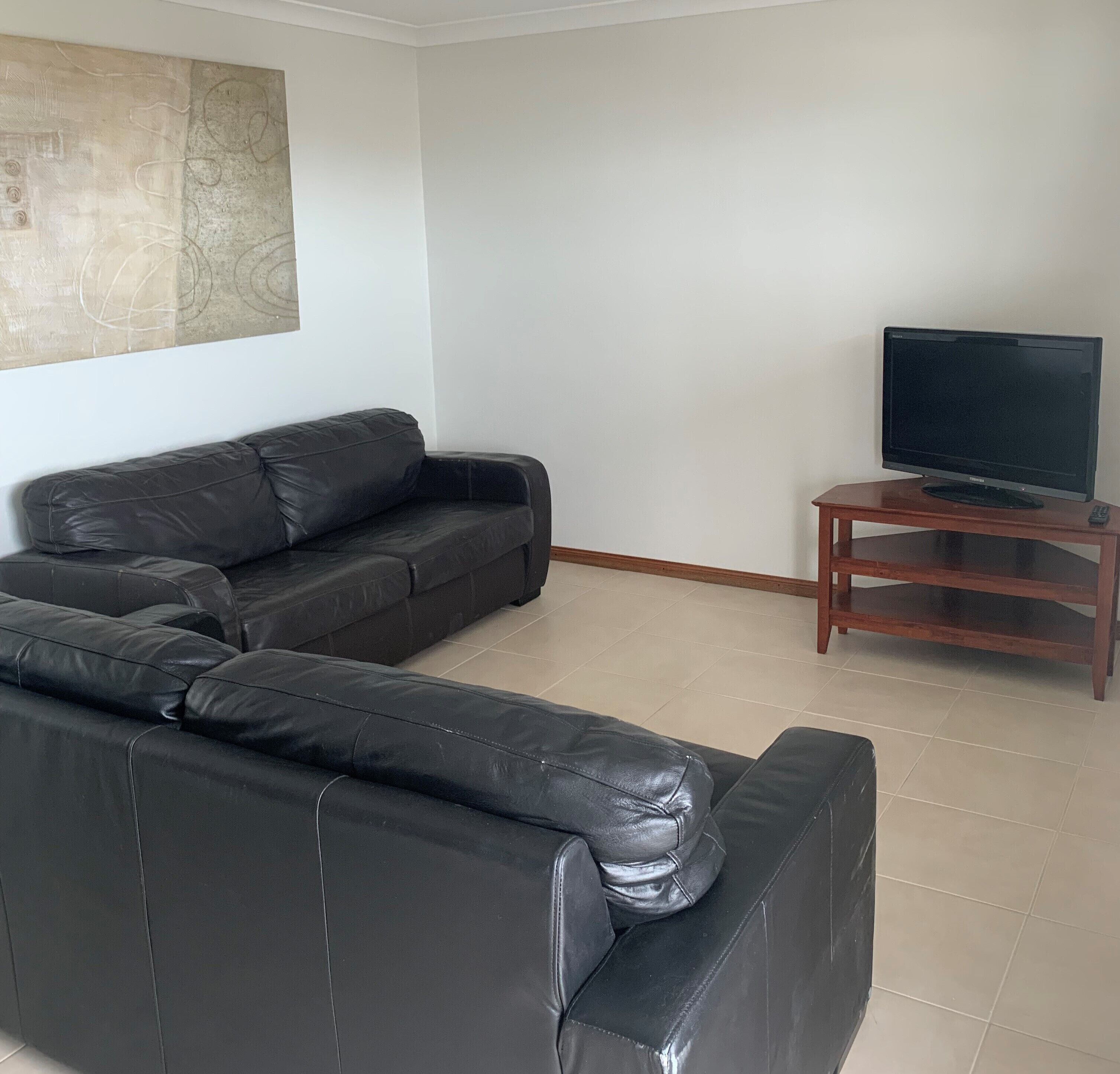 A living room with a black leather sofa, a wooden TV stand, and a large abstract painting on the wall.