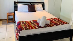 A neatly made bed with a striped blanket, a wooden bedside table, and a wall-mounted air conditioner. - Airlie Beach Apartments (Airlie Beach)