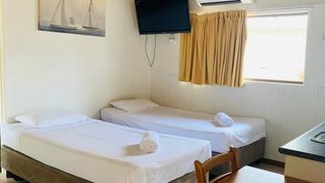 A room with two beds, a ceiling fan, a mounted TV, and a window with curtains.