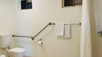 Un baño con inodoro, una ventana pequeña, cortina de ducha y barra de apoyo.