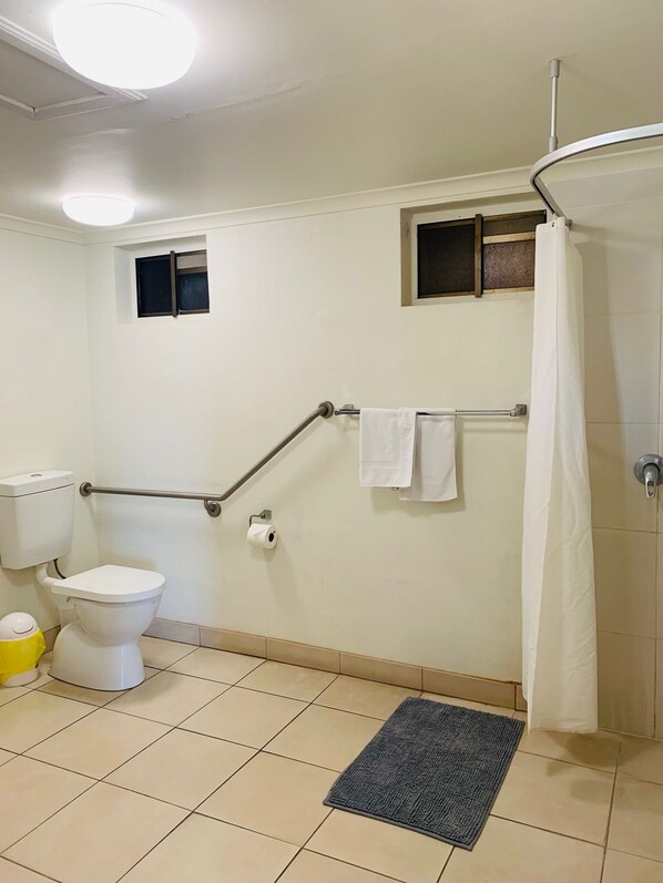 Une salle de bain équipée de toilettes, d’une petite fenêtre, d’un rideau de douche et d’une barre d’appui.