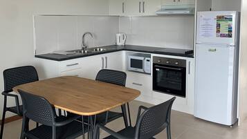 A modern kitchen with white cabinets, a built-in oven, a microwave, and a refrigerator. There is a wooden table with four chairs.