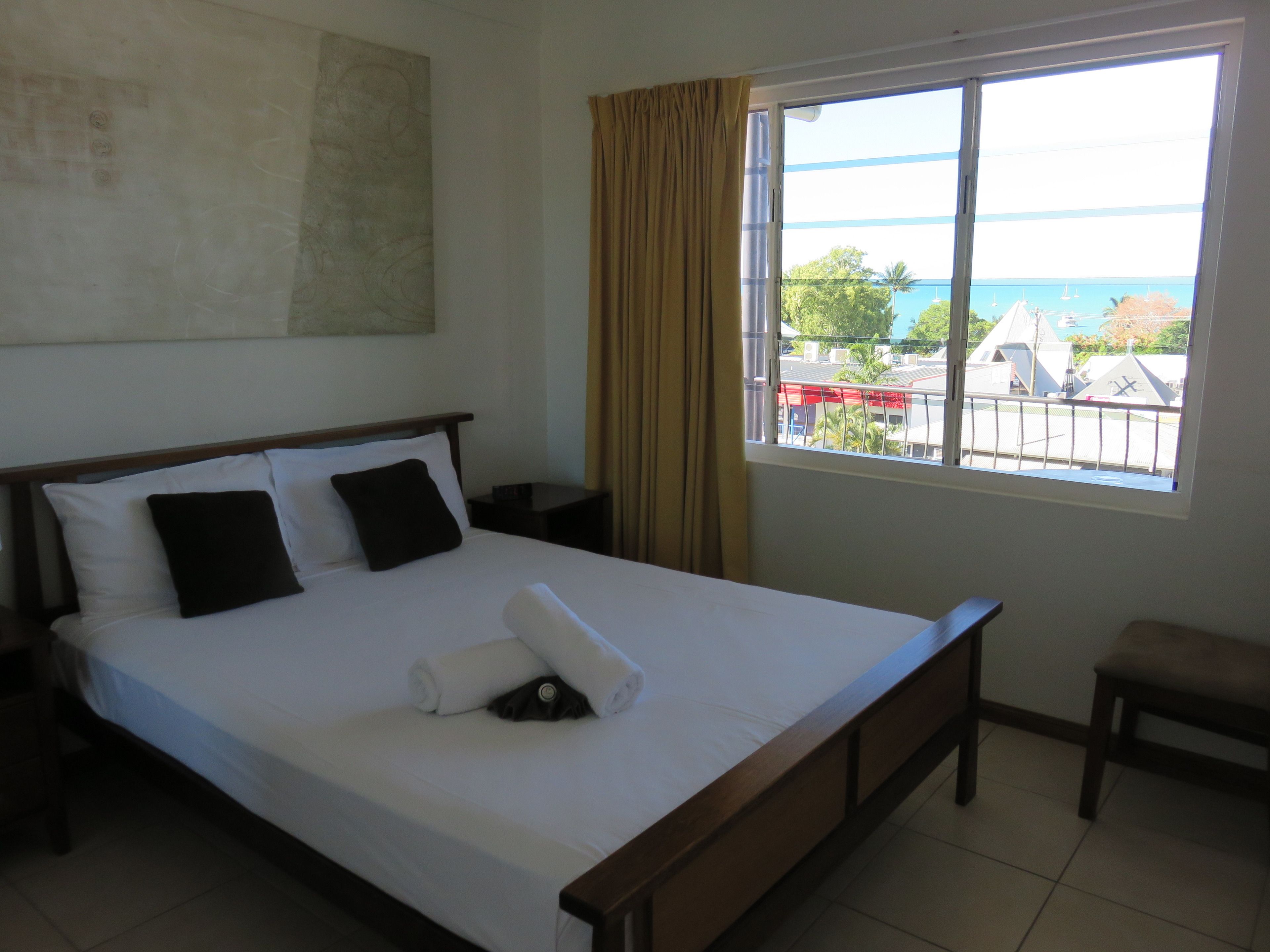 A hotel room with a large bed, a nightstand, a chair, a window with a view of buildings and the sea.