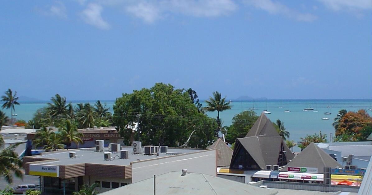 A coastal town with buildings, palm trees, and a clear view of the ocean.