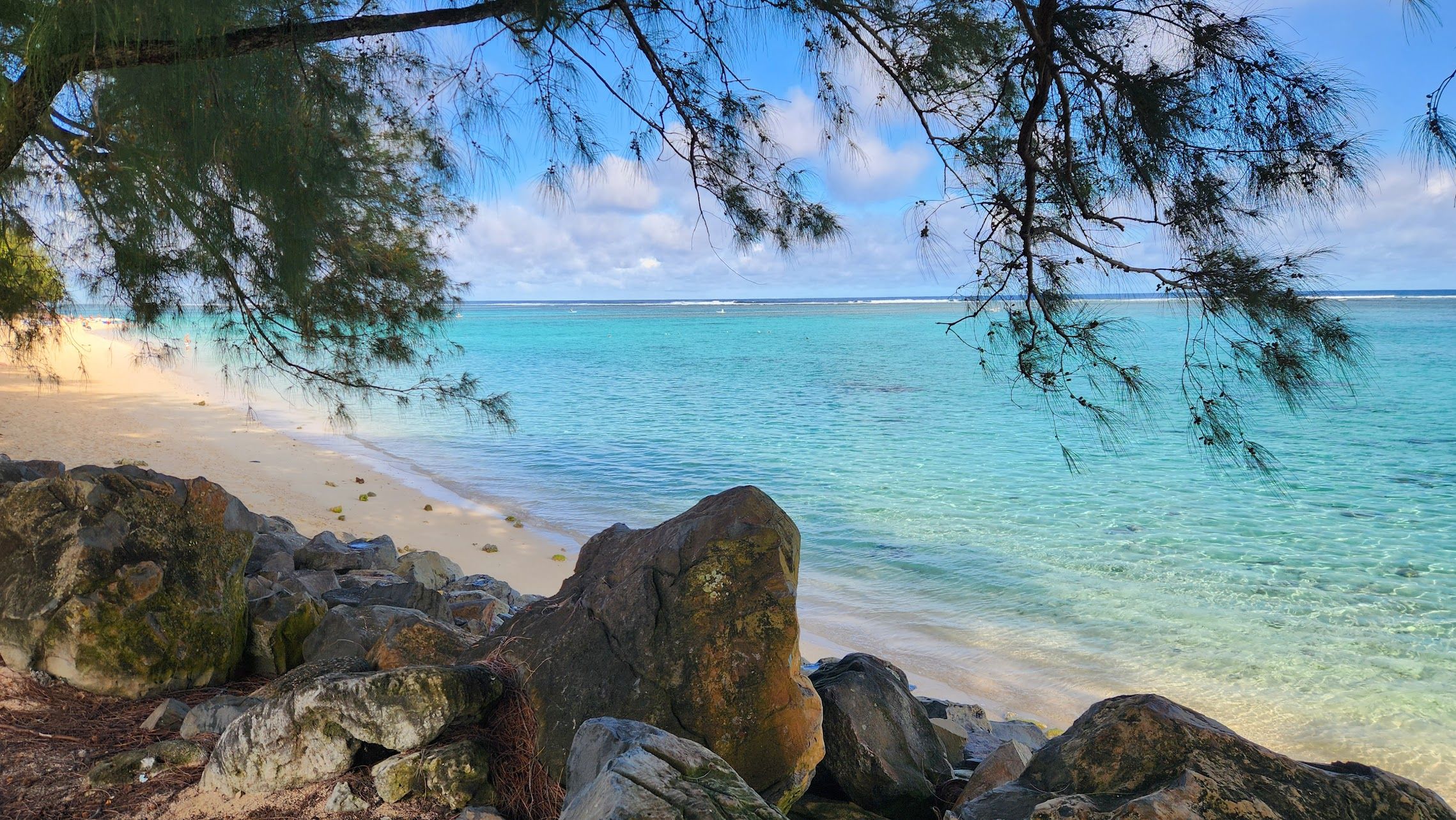 Ein Strand mit klarem türkisblauem Wasser, sandigem Ufer und großen Felsen.