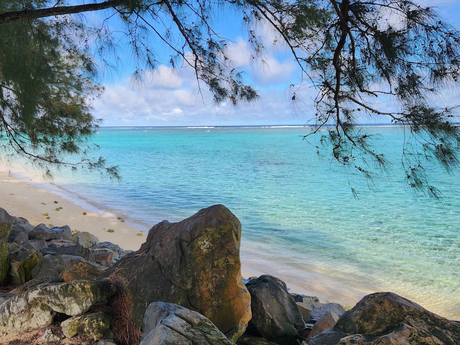 A beach with clear turquoise water, sandy shore, and large rocks.