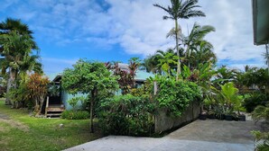 A tropical garden with a house, palm trees, and a variety of plants. - Aroa Kainga Bungalows (Rarotonga)