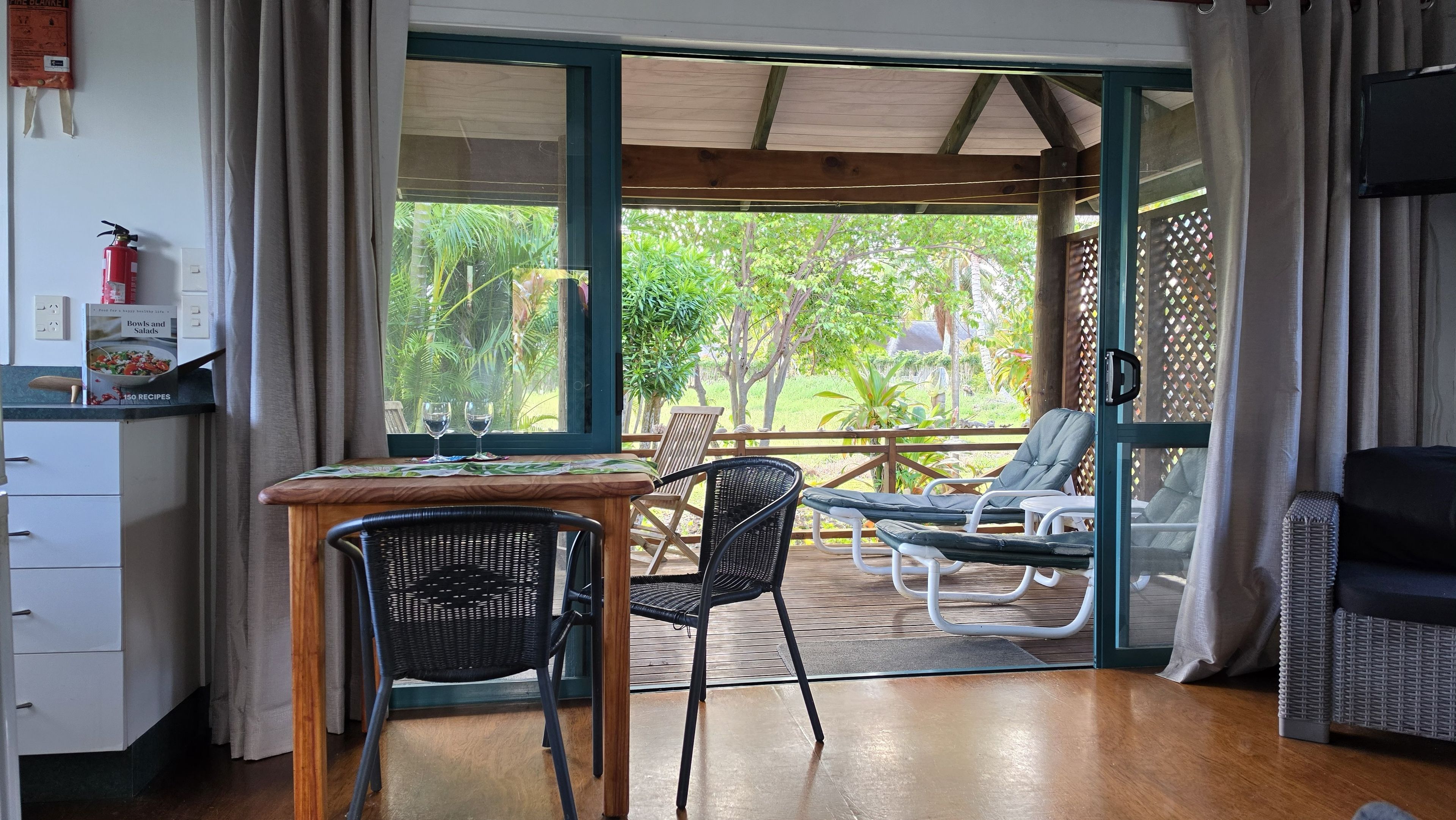 Una habitación con una mesa de comedor, sillas, un sofá y vistas de un jardín a través de un ventanal.
