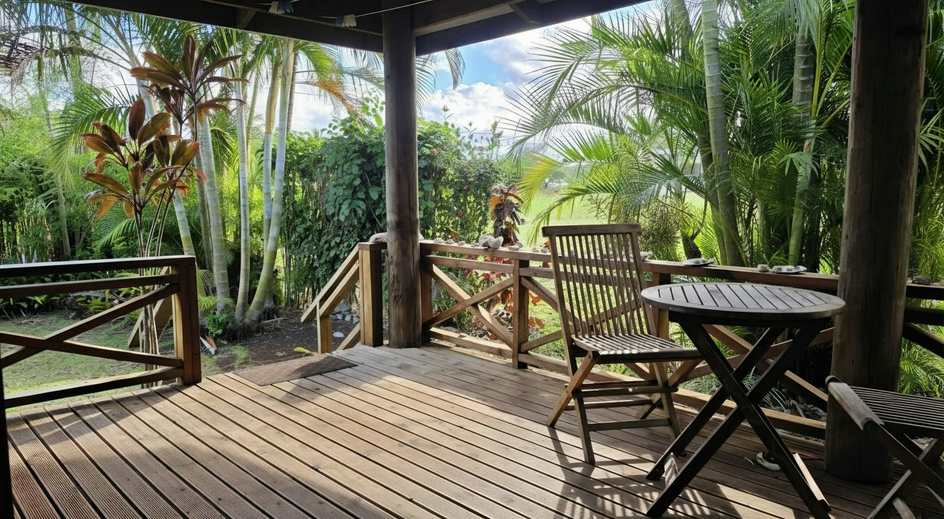Una terraza de madera con mesa y sillas, rodeada de exuberante vegetación tropical.