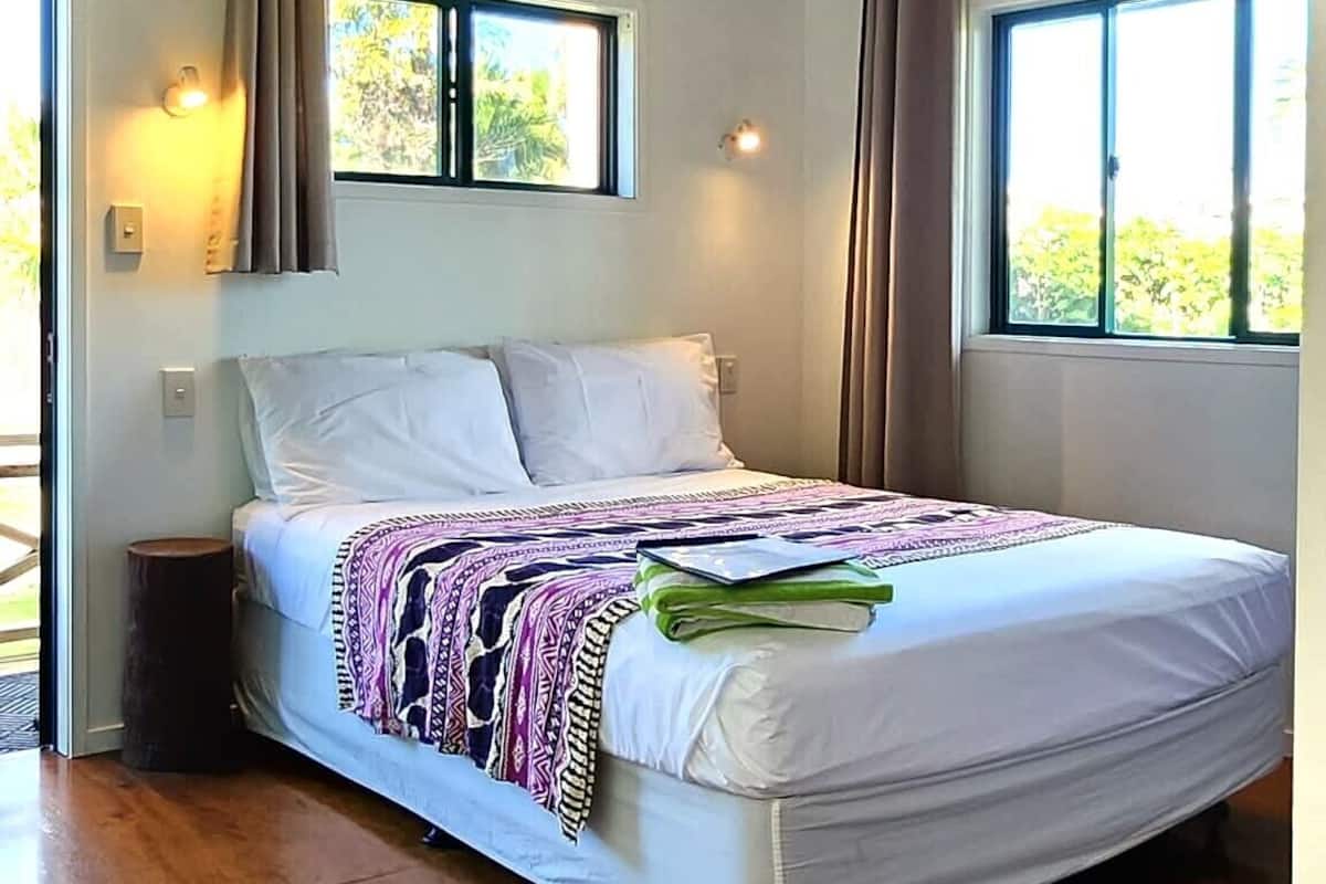 A bedroom with a bed, ceiling fan, windows, and a view of greenery outside.