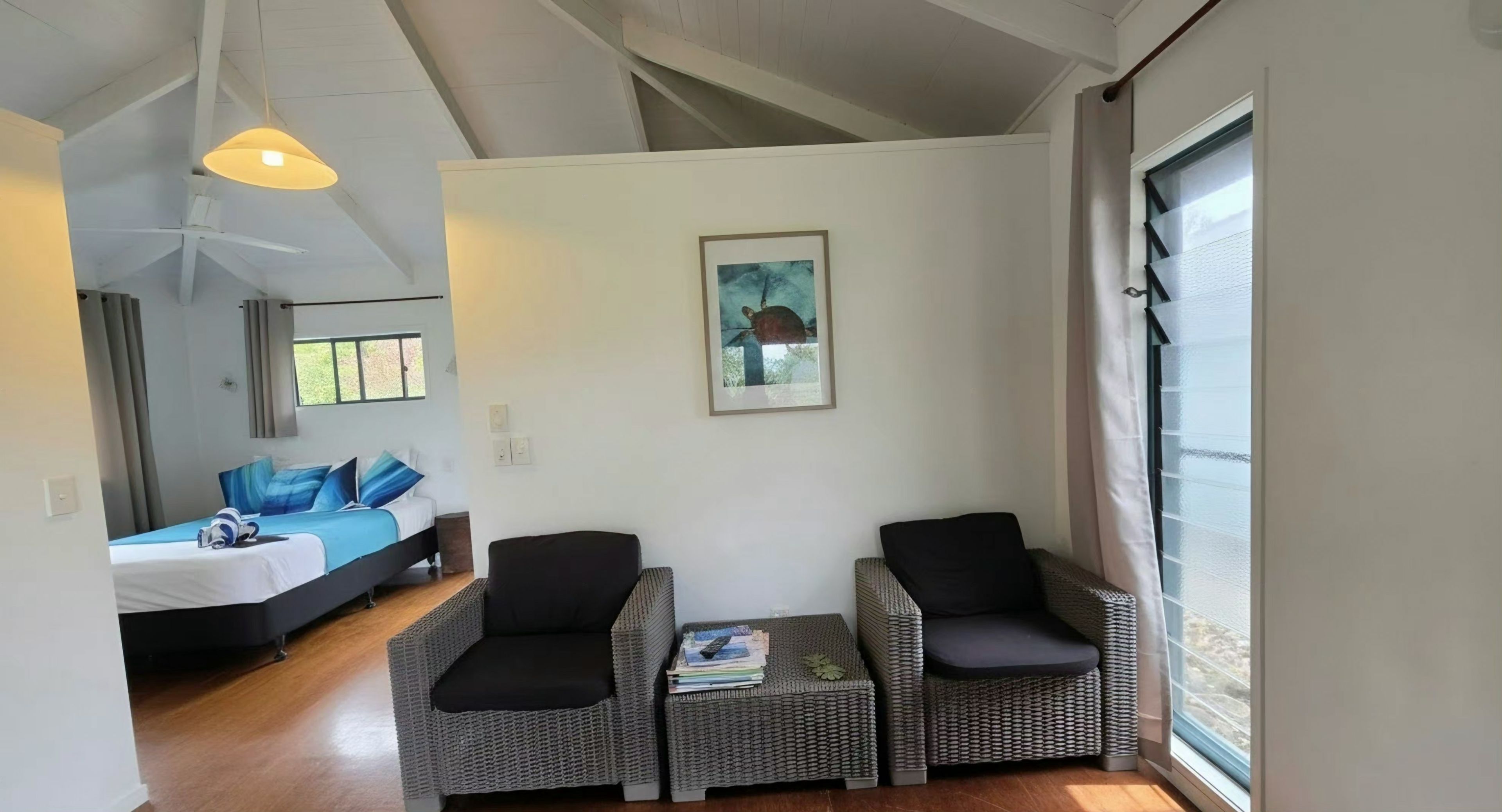 Quarto com cama, duas cadeiras, uma mesa pequena e janela com vista.