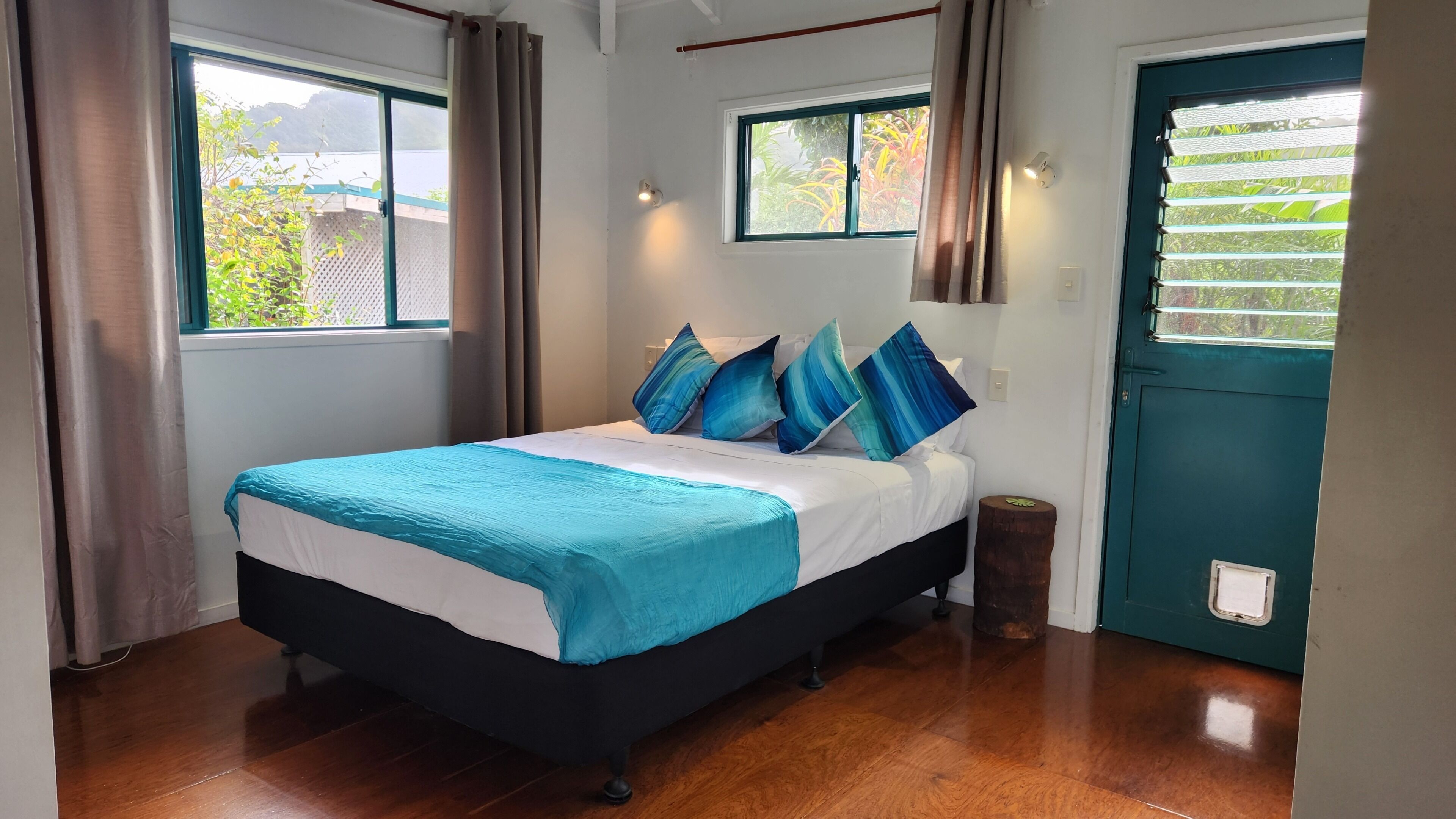 Ein Schlafzimmer mit Bett, Vorhängen, Fenstern und einer Tür.