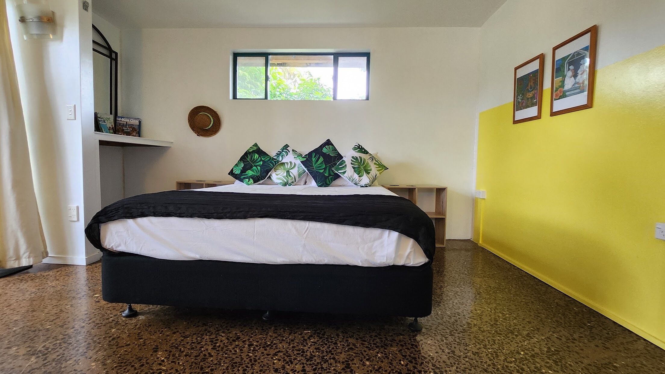 Quarto com cama, janela, parede com quadros e parede amarela.