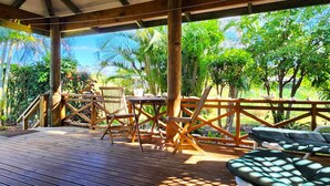 A wooden deck with a table and chairs, surrounded by lush greenery and palm trees. - Aroa Kainga Bungalows (Rarotonga)