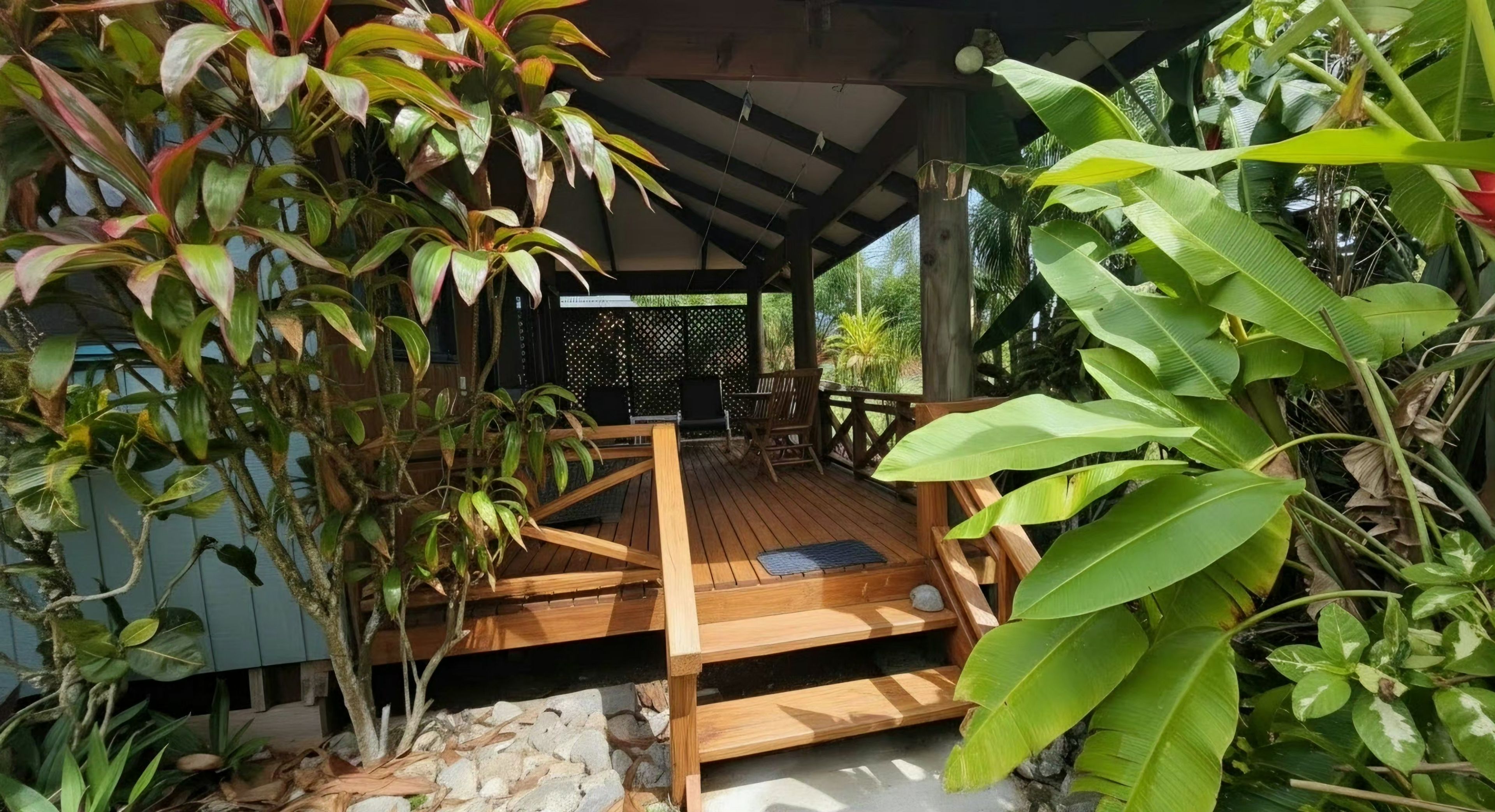 Une terrasse en bois dotée d’un espace salon abrité, entourée d’une végétation luxuriante.