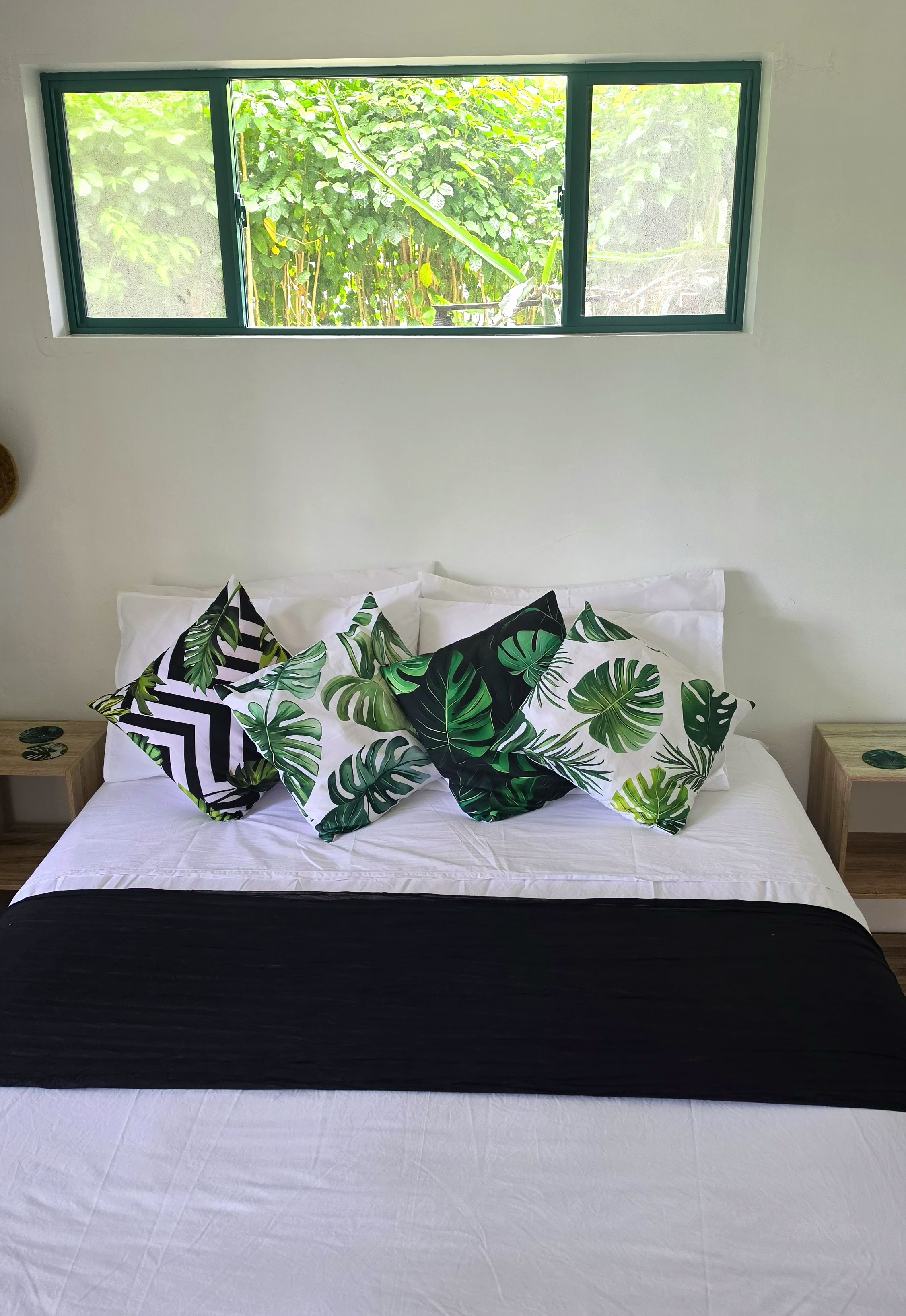 A bed with white bedding and multiple pillows with tropical leaf patterns.