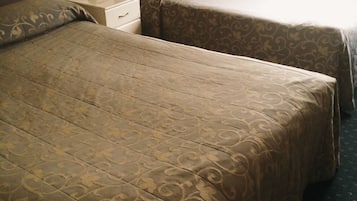 A hotel room with a large bed, two single beds, a nightstand, a lamp, and a window with a view of trees.