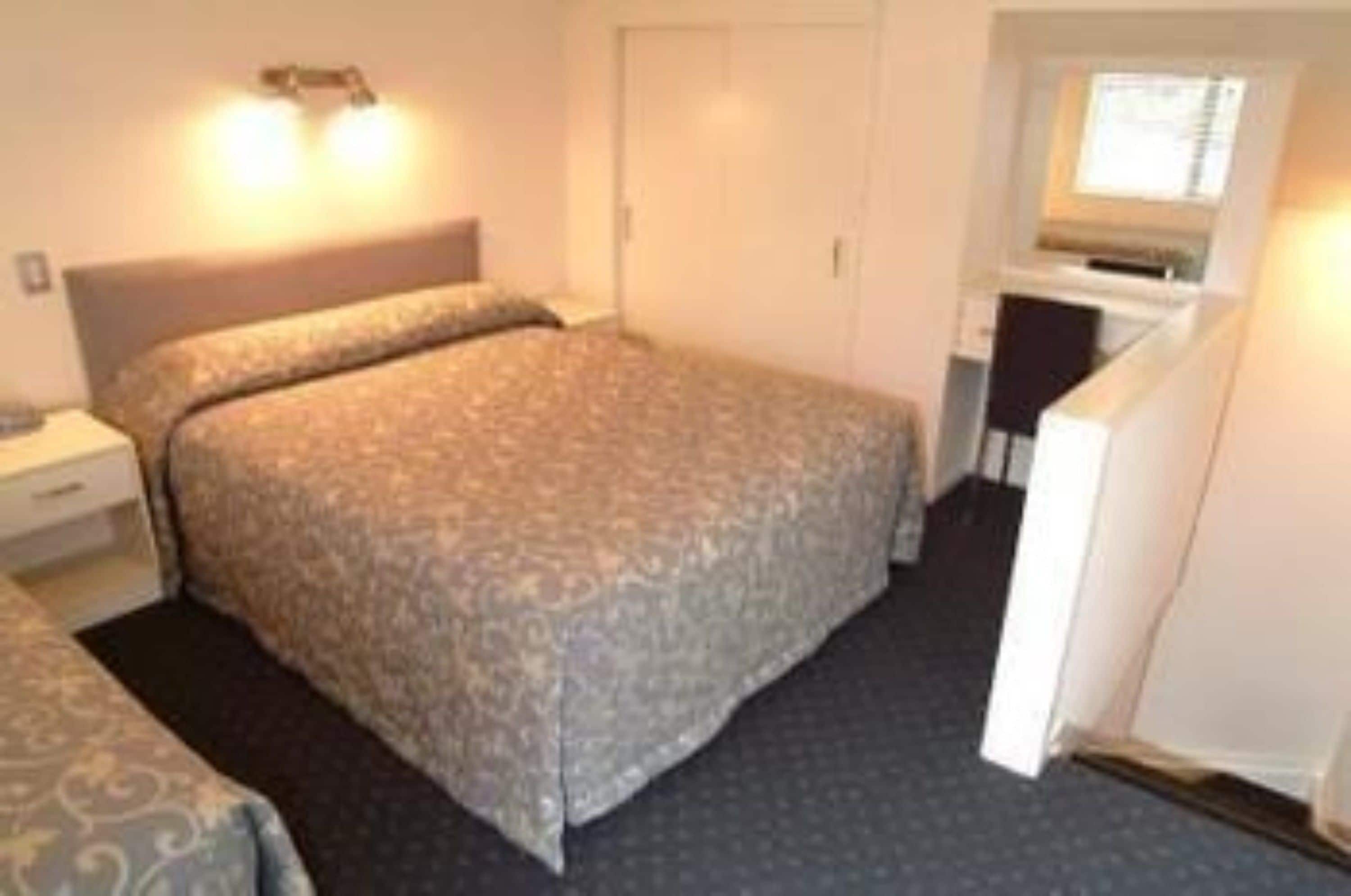 Un dormitorio pequeño y ordenado con cama, mesita de noche y ventana.