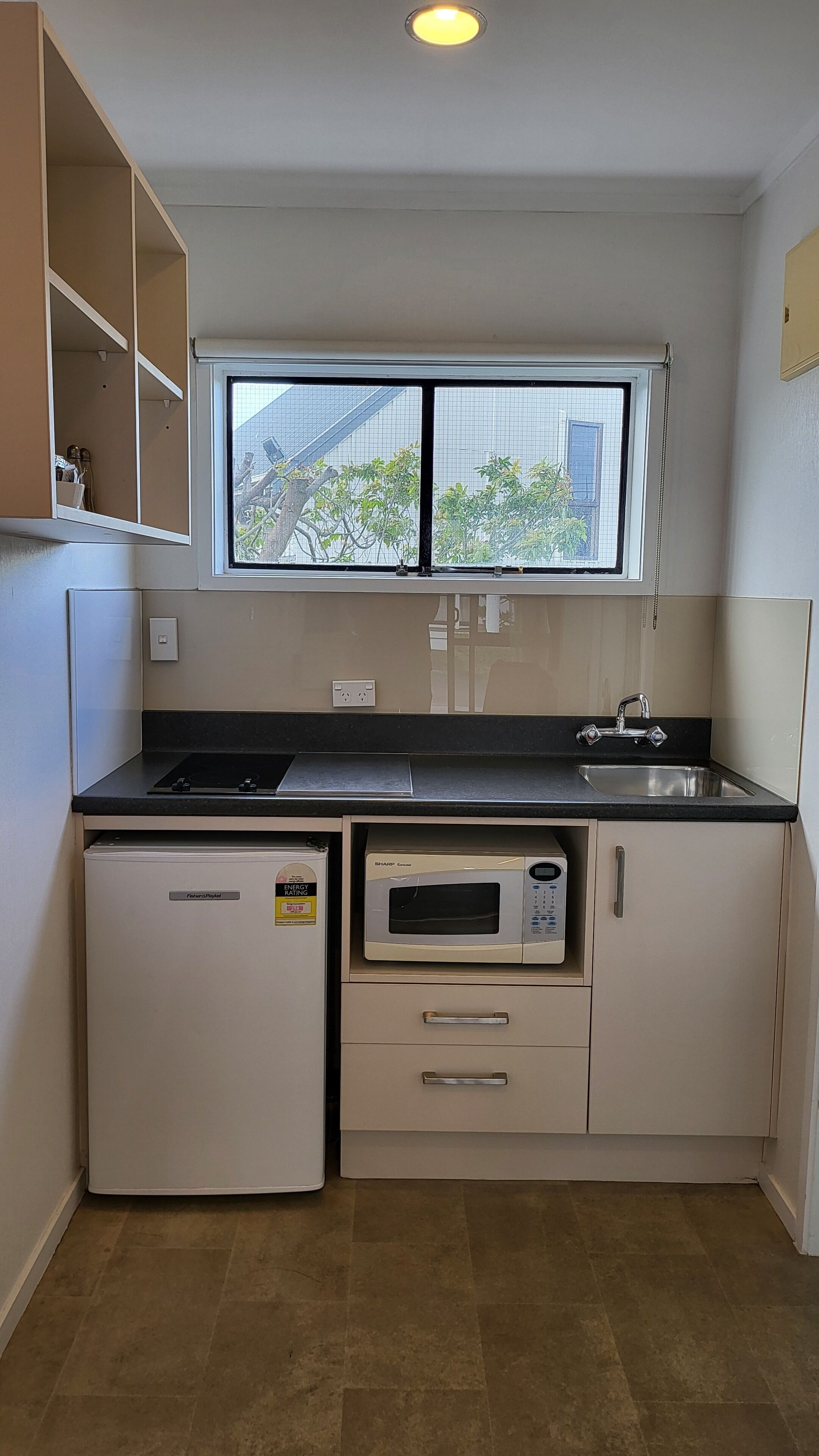 Una cocina compacta con microondas integrado, un lavabo y un refrigerador pequeño.