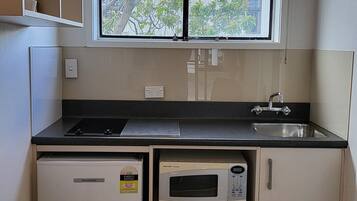Una cocina compacta con microondas integrado, un lavabo y un refrigerador pequeño.